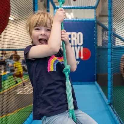 A young girl smiling whilst sat on a rope swing inside the AeroPlay soft play area.